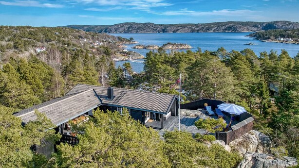 Une cabane moderne dotée d’un toit en pente, entourée d’une forêt dense et offrant une vue sur un lac parsemé de formations rocheuses.