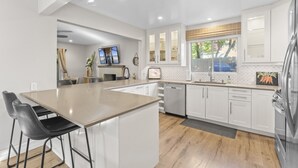 A modern kitchen with white cabinetry, a central island, and a built-in oven. - Hideaway A- Walk to the beach, Downtown, AC! (San Clemente)