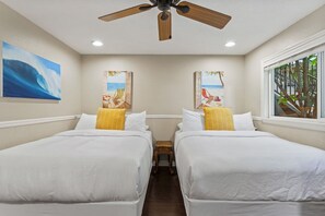 Une chambre d’hôtel avec deux lits, un ventilateur de plafond et des œuvres d’art représentant des scènes de plage.