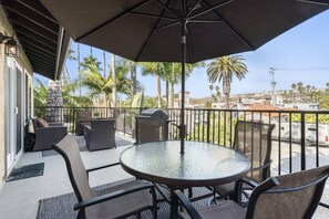 Un balcon avec une table ronde en verre, des chaises en osier et un grand parasol.