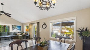Ein Essbereich mit Holztisch, vier Stühlen, einer Chandelierleuchtre, einer Uhr und Blick ins Freie durch ein großes Fenster.