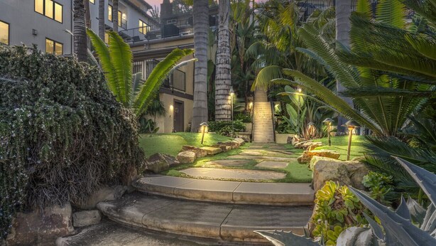 Ein angelegter Garten mit einem Kiesweg, der zu einer Treppe führt, umgeben von tropischen Pflanzen und Palmen.