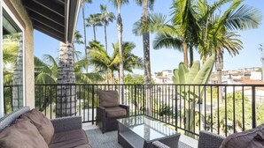 Ein Balkon mit Rattanmöbeln, einem Glastisch und Blick auf Palmen und Gebäude.