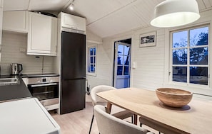 A modern kitchen with white cabinets, a black refrigerator, a wooden dining table, and a large window. - Nice home in Nevlunghavn with WiFi (Nevlunghavn)