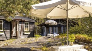 Eine rustikale Holzhütte mit einer kleinen Veranda und einem Tisch mit Stuhl unter einem großen Sonnenschirm.