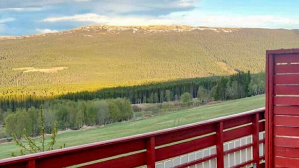 A view from a red-framed balcony overlooking a forested hillside with a clear sky. - Cozy home in Oppdal with house a mountain view (Oppdal)
