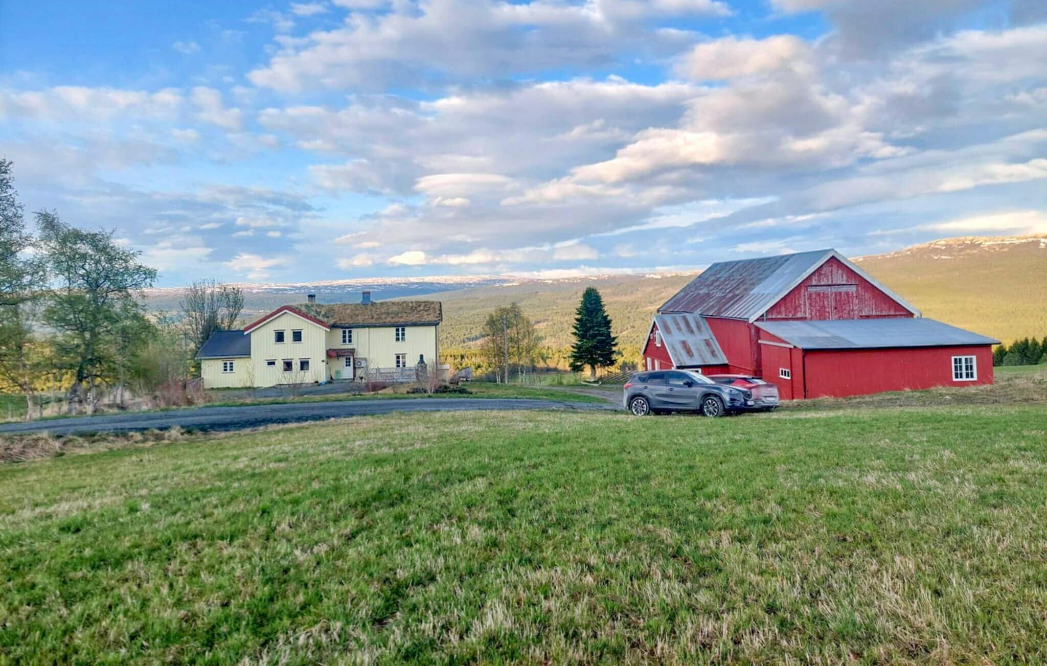 A rural landscape with a red barn, two houses, and a car parked in front.
