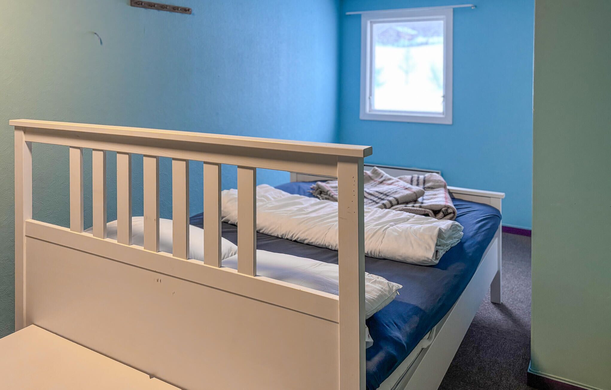 A single bed with a white headboard and blue mattress in a room with blue walls and a window.