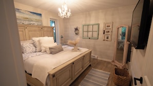 Quarto com cama grande, lustre, espelho e piso de madeira.