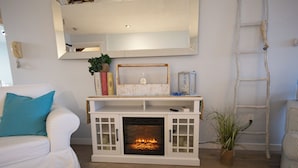 Uma sala de estar com lareira, móveis brancos e um espelho na parede.