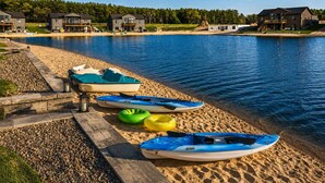 A lakeside property with a dock, kayaks, and a sandy beach.