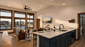 A modern kitchen with a large island, wooden flooring, and a view of the water through large windows.