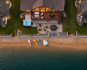Luftaufnahme eines Hauses mit Terrasse, Whirlpool, Sitzgelegenheit im Freien und Kajaks am Wasser.