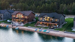A lakeside property with multiple houses, a dock with kayaks, and a forested backdrop.