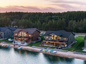 En ejendom ved søen med flere huse, en dock med kajakker og skov i baggrunden.