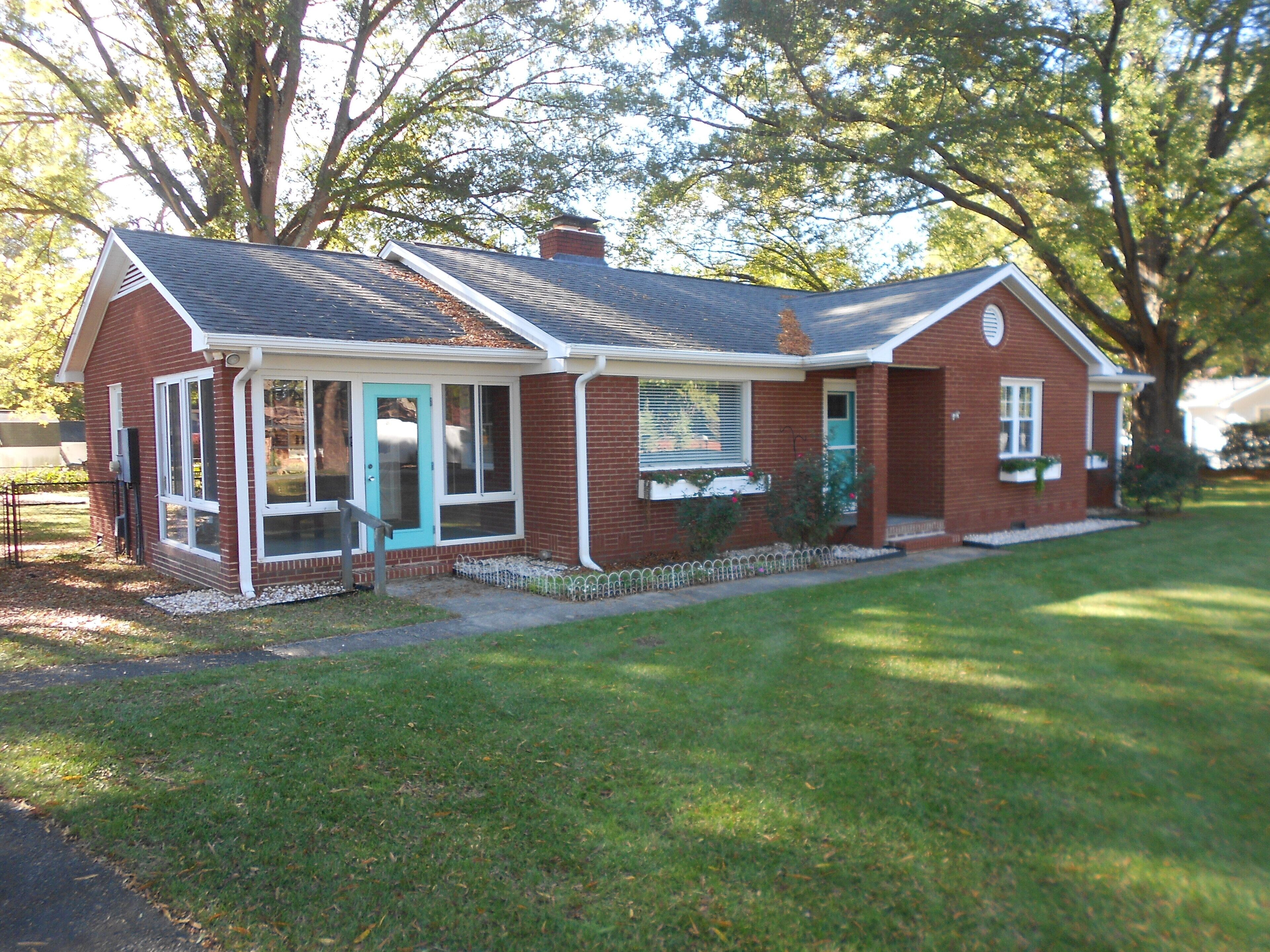 A single-story brick house with a gabled roof, a front porch, and a small front yard.