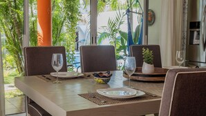 Uma sala de jantar com uma mesa posta para dois, cadeiras e vista para plantas tropicais lá fora.