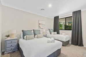A hotel room with two beds, a nightstand with a lamp, a painting on the wall, and a window with curtains. - Sun-Drenched. Brand-New Home. Sleeps 11 (Green Point)