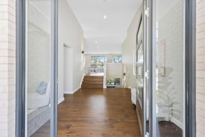 A modern hallway with a wooden floor, glass doors, and a staircase leading to a dining area. - Ruby Lodge by Coast Hosting (Green Point)
