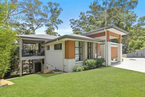 A modern two-story house with a covered patio, a small garden, and a view of surrounding trees. - Sun-Drenched. Brand-New Home. Sleeps 11 (Green Point)