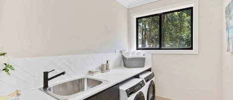 Un moderno lavadero con lavabo, lavadora y ventana con vistas a árboles.