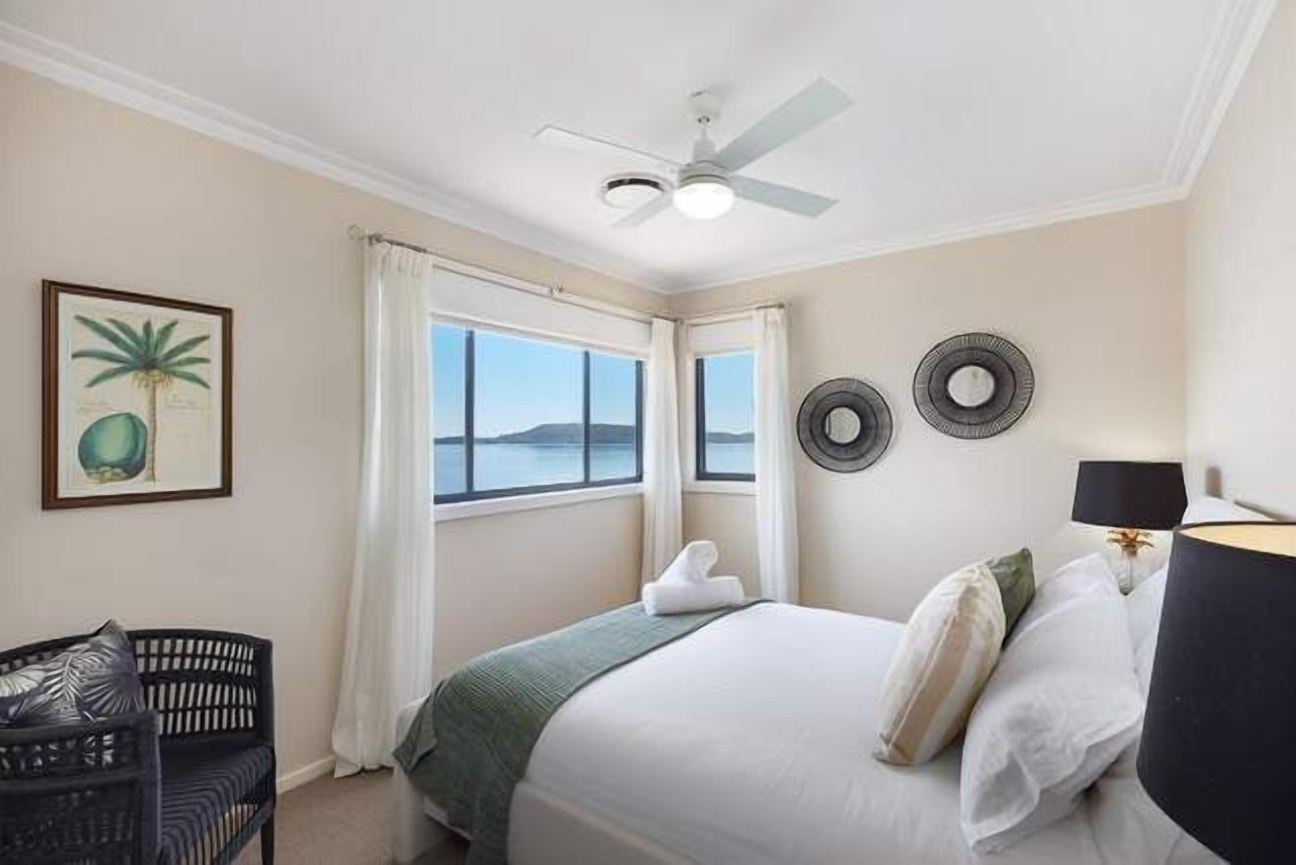 Une chambre à coucher avec un lit, une chaise, un ventilateur de plafond et une fenêtre avec des rideaux.