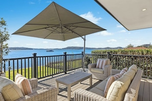 A deck with wicker furniture, a table, and an umbrella. - Waters Edge by Coast Hosting (Koolewong)