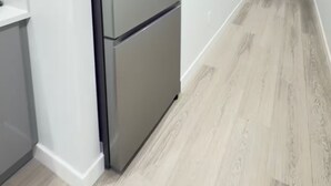 A modern kitchen with a stainless steel refrigerator, white walls, and light wood flooring. - Zillion’s Bliss - Basement Suite (Calgary)