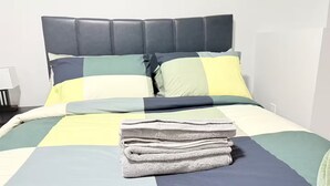 A neatly made bed with a striped bedspread, a stack of folded towels, and a headboard. - Zillion’s Bliss - Basement Suite (Calgary)