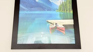 A framed landscape painting of a mountain lake with a dock and canoe. - Zillion’s Bliss - Basement Suite (Calgary)