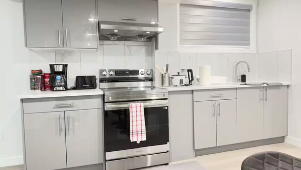 A modern kitchen with stainless steel appliances, white cabinetry, and a window above the sink. - Zillion’s Bliss - Basement Suite (Calgary)
