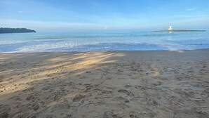 A beach with footprints leading to the water, a lighthouse on a small island, and a distant landmass. - Private 2 Bedrooms Villa Near Waterfall in Khao Lak-terrace Large Bubble Jacuzzi (Takua Pa)
