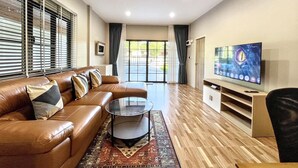 A modern living room with a leather sofa, a glass coffee table, a flat-screen TV, and a view through a glass door. - Private 2 Bedrooms Villa Near Waterfall in Khao Lak-terrace Large Bubble Jacuzzi (Takua Pa)
