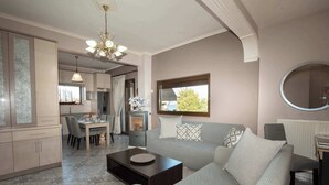 A modern living room with a sofa, coffee table, and a dining area with chairs and a table. - Sunrise Suite Olympiada - Luxury Beachfront Escape (Aristotelis)