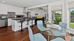 Una cucina moderna con mobili bianchi, un'isola centrale con sgabelli da bar e un tavolo da pranzo in vetro con sedie azzurrine.