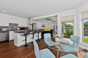A modern kitchen with white cabinets, a central island with bar stools, and a glass dining table with light blue chairs. - Lakefront Home with Hot Tub, Private Dock & Ramp (Hot Springs)