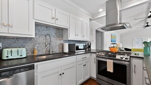Una cucina moderna con mobili bianchi, una lavastoviglie in acciaio inossidabile, un forno a microonde, un fornello e una ventola a soffitto.