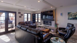 A modern living room with a leather sofa, a fireplace, and a large TV.