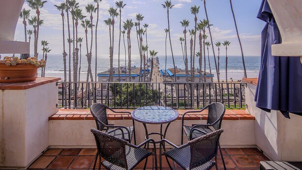 A balcony with a view of the beach, palm trees, and a tiled floor.