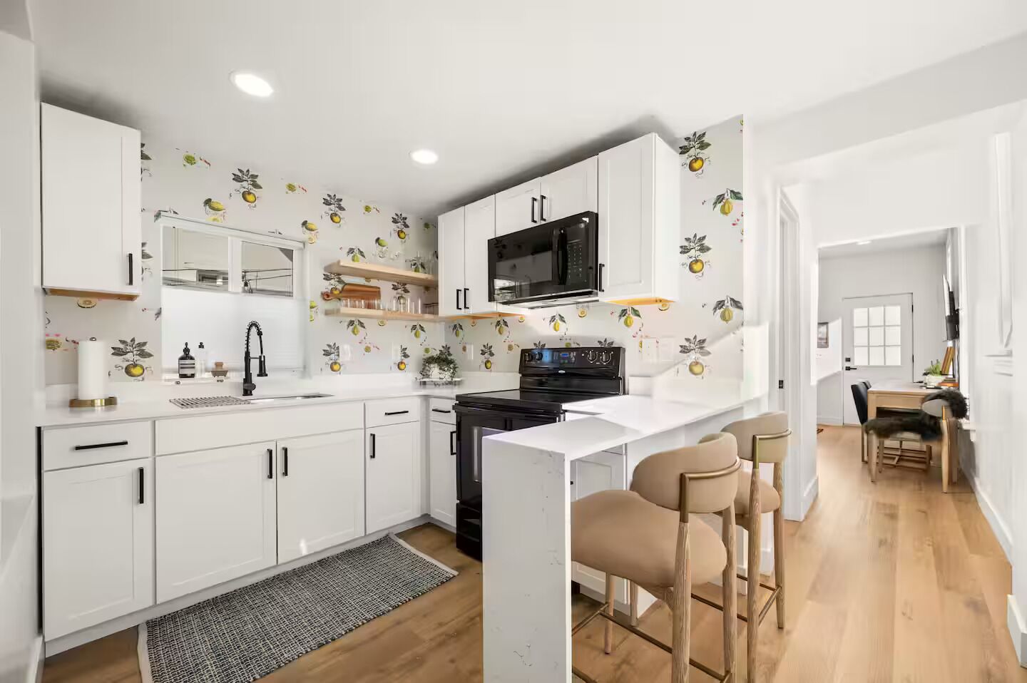Una cocina moderna con armarios blancos, un microondas negro y un comedor de madera.