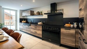 A modern kitchen with a central island, built-in oven, and stainless steel appliances. - La Ferme Geromoise - Gathering and exploring the Vosges - OVO Network (Gérardmer)