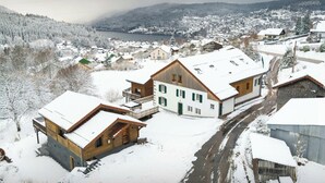 A snow-covered village with traditional wooden houses, a river, and a mountain backdrop. - La Ferme Geromoise - Gathering and exploring the Vosges - OVO Network (Gérardmer)