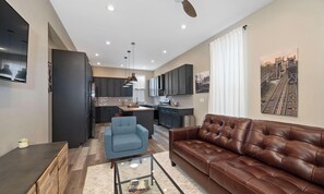 A modern kitchen with dark cabinets, a blue chair, and a brown leather sofa. - Stylish Townhouse with Game Room, King Suite (Cincinnati)