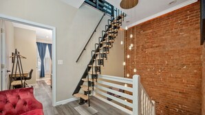 A staircase with a white railing, a red sofa, and a brick wall. - Stylish Townhouse with Game Room, King Suite (Cincinnati)