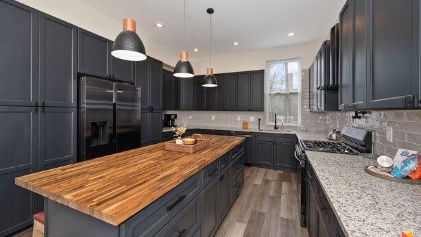 A modern kitchen with dark cabinetry, a wooden island, stainless steel appliances, and pendant lighting. - Stylish Townhouse with Game Room, King Suite (Cincinnati)