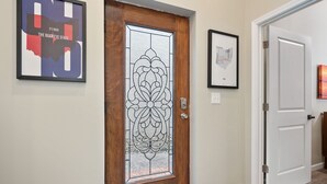 A hallway with a wooden door featuring a decorative glass panel, a framed map on the wall, and a white door to the right. - Stylish Townhouse with Game Room, King Suite (Cincinnati)