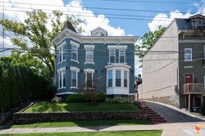 A two-story house with a green facade, white trim, and a stone foundation. - Stylish Townhouse with Game Room, King Suite (Cincinnati)