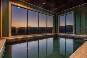 Ein Schwimmbad mit großen Fenstern, die einen Blick auf einen Sonnenuntergang über den Bergen bieten.