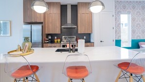 A modern kitchen with wooden cabinets, a central island with bar stools, and pendant lighting. - OmAura Home vibe | Austin Downtown | Games | 4BR (Austin)