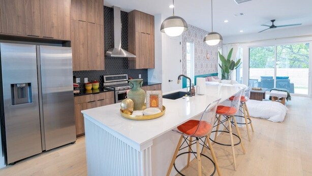 A modern kitchen with stainless steel appliances, wooden cabinets, and a central island with bar stools. - OmAura Home vibe | Austin Downtown | Games | 4BR (Austin)